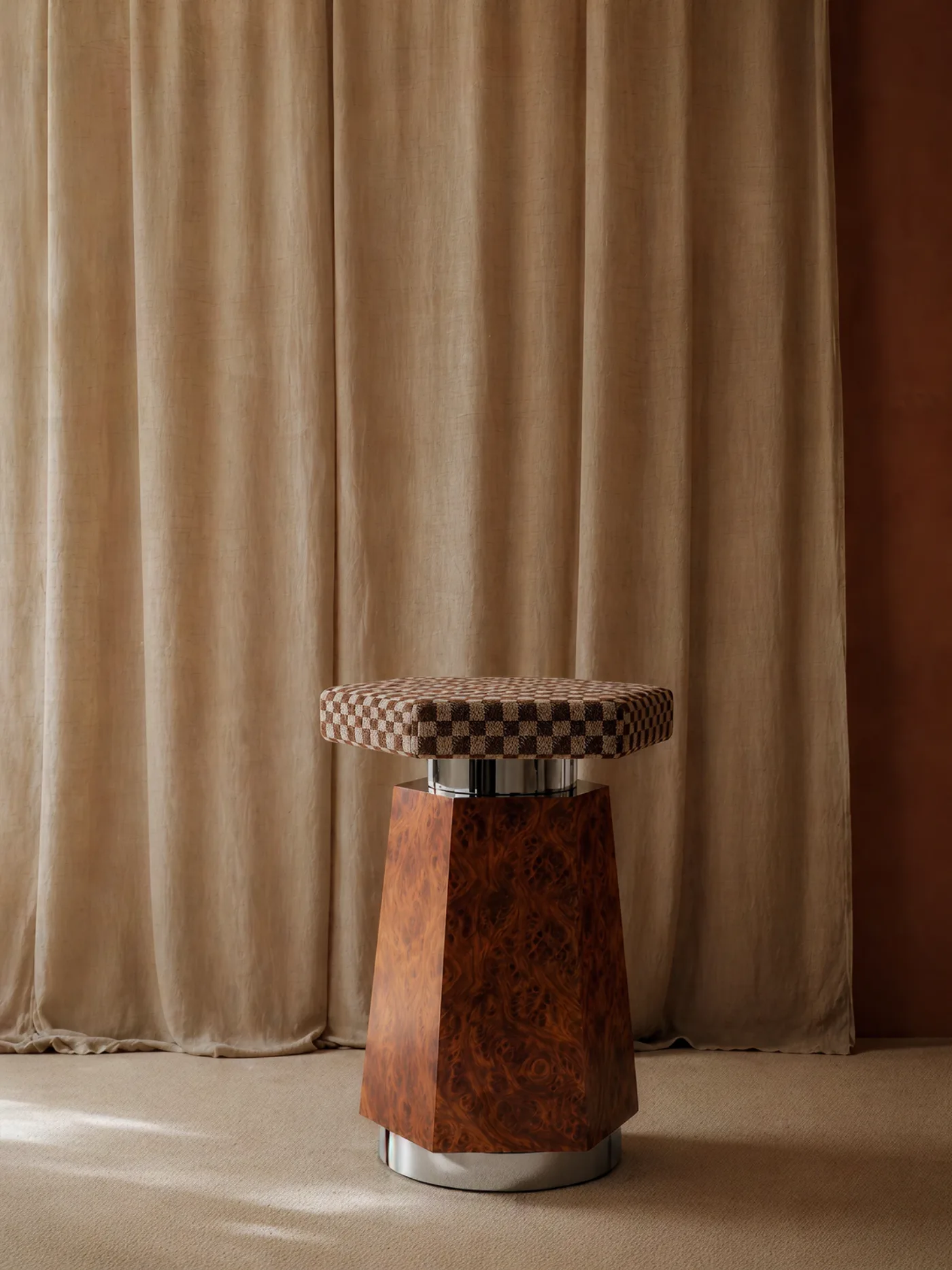 Le tabouret : socle facetté en ronce de noyer, anneau chromé et assise en bouclé damier